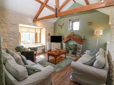 A living room with two sofas a wooden coffee table a fireplace and exposed wooden ceiling beams at Beudy in Chwilog