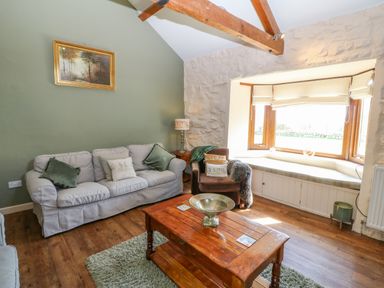 A living room with a sofa, armchair, wooden coffee table, window seat, and a framed picture on a green wall at Beudy in Chwilog