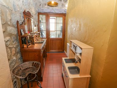 A narrow room with a vintage wooden dresser and stool on one side and a small wooden play kitchen on the other at Beudy in Chwilog