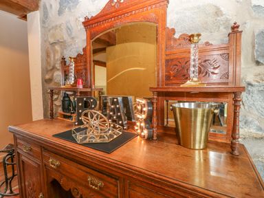A wooden sideboard with decorative mirror letters spelling bar a gold bucket and stone wall at Beudy in Chwilog
