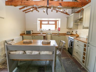 A kitchen with wooden table and bench seating under exposed wooden ceiling beams at Beudy in Chwilog