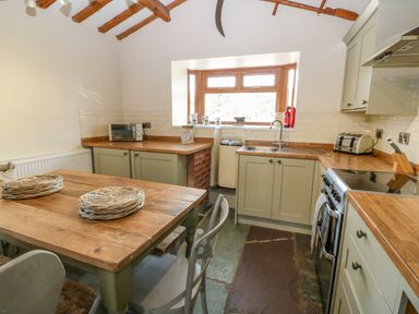 A kitchen with wooden countertops a dining table with woven placemats and exposed wooden beams at Beudy in Chwilog