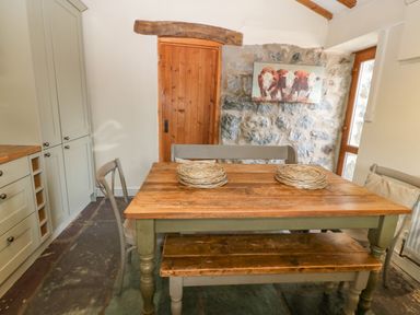 A dining area with a wooden table bench and chairs stone wall and wooden door at Beudy in Chwilog