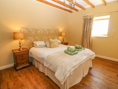 A bedroom with a double bed two bedside tables with lamps and a window with curtains at Beudy in Chwilog