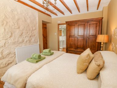 A bedroom with a bed with green towels and pillows a wooden wardrobe and a lamp at Beudy in Chwilog
