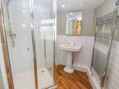 A bathroom with a shower enclosure pedestal sink mirror and heated towel rail at Beudy in Chwilog