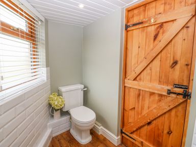 A bathroom with a toilet a wooden door and a vase with flowers at Beudy in Chwilog