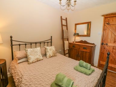 A bedroom with a double bed pillows ladder with towels wooden dresser mirror and wooden door at Beudy in Chwilog