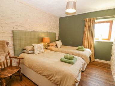 A bedroom with two single beds a wooden chair and a window with curtains at Beudy Chwilog