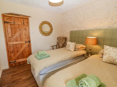 A bedroom with two single beds a wooden door a round mirror and a wooden chair with a fur throw at Beudy in Chwilog