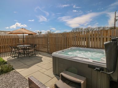 An outdoor patio with a hot tub and a table with chairs and an umbrella at Beudy in Chwilog