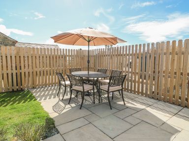 An outdoor patio with a round table six chairs and a large umbrella enclosed by a wooden fence at Beudy in Chwilog