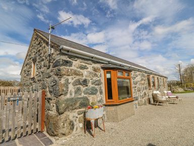 Stone house with wooden windows and outdoor seating area at Beudy in Chwilog