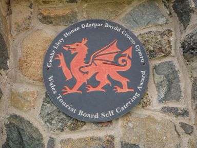 A circular plaque with a red dragon and text mounted on a stone wall at Beudy in Chwilog