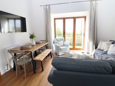 A living room with a wooden dining table chairs a bench a blue armchair and two blue sofas at Sgubor in Chwilog