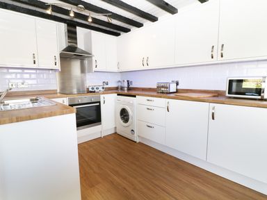 A kitchen with white cabinets wooden countertops and appliances at Sgubor in Chwilog