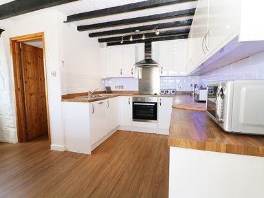 A kitchen with white cabinets wooden countertops appliances and wooden door at Sgubor in Chwilog