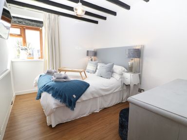 A bedroom with a bed bedside tables lamps a window and a wooden floor at Sgubor in Chwilog