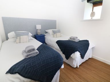 A bedroom with two single beds side by side a blue nightstand with a lamp between the beds and towels placed on each bed at Sgubor in Chwilog