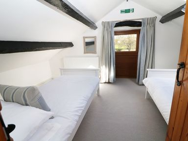 A bedroom with two single beds a window with curtains and exposed ceiling beams at Sgubor in Chwilog