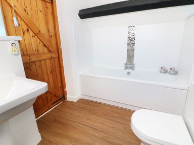 A bathroom with a wooden door a white bathtub with two rubber ducks a white sink and a toilet at Sgubor in Chwilog