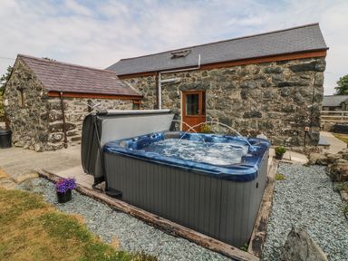 An outdoor hot tub with water jets in front of a stone building with a wooden door at Sgubor in Chwilog