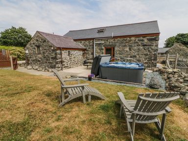 A stone house with a garden featuring two wooden chairs a hot tub and a picnic table at Sgubor in Chwilog