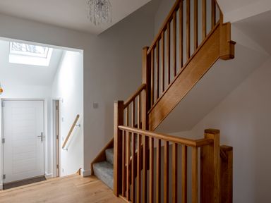 A staircase with wooden railing and carpeted steps next to a white door with a glass skylight above at Godrevy in St Ives