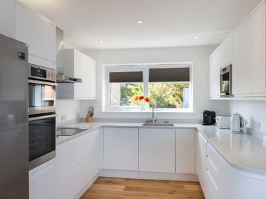 A kitchen with white cabinets stainless steel appliances and a window with flowers at Godrevy in St Ives