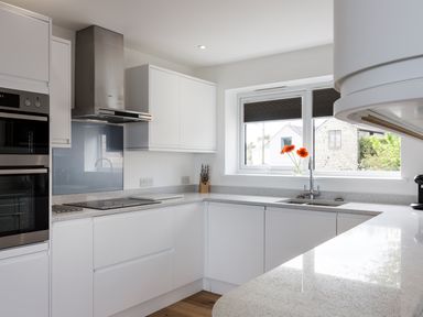 A kitchen with white cabinets a stove oven a sink and orange flowers on the windowsill at Godrevy in St Ives