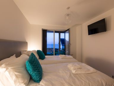 A bedroom with two beds blue pillows towels on beds wall mounted tv and a glass door opening to an outside view at Godrevy in St Ives