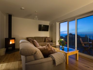 A living room with sofas a wood burning stove and glass doors opening to a balcony at Godrevy in St Ives