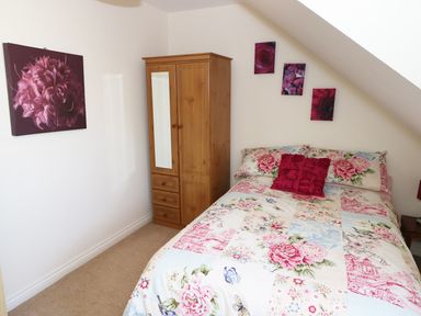 A bedroom with a floral bedspread a wooden wardrobe and floral wall art at 5 Chandlers Yard in Burry Port