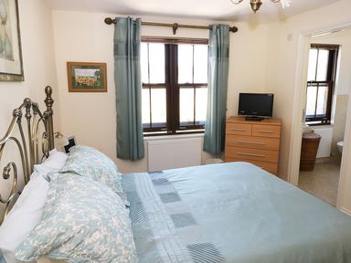 A bedroom with a metal bed frame light blue bedding wooden chest of drawers with a small TV and window with blue curtains at 5 Chandlers Yard in Burry Port