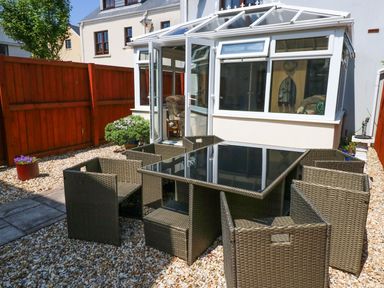 An outdoor patio with a glass table and eight wicker chairs next to a conservatory at 5 Chandlers Yard in Burry Port