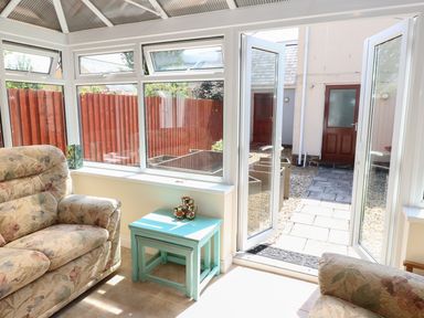 A conservatory with floral armchairs a small blue nested table and open doors leading outside at 5 Chandlers Yard Burry Port