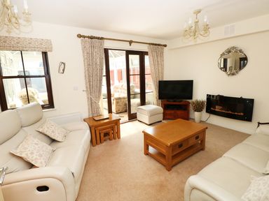A living room with beige sofas a wooden coffee table a television and a wall-mounted fireplace at 5 Chandlers Yard in Burry Port
