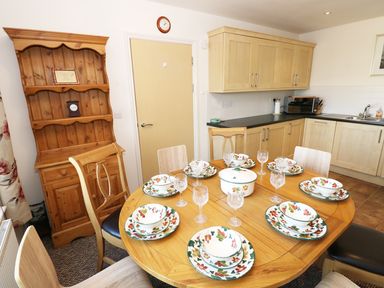 A kitchen with wooden cabinets a wooden dining table set with plates bowls and glasses at 5 Chandlers Yard in Burry Port