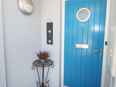 A blue front door with a round window and number 5 next to a metal table with a plant and a welcome sign at 5 Chandlers Yard in Burry Port
