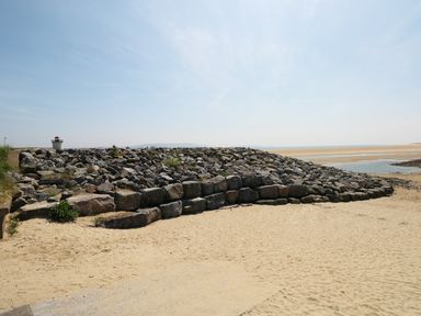 A sandy beach with a rock jetty and a small lighthouse at 5 Chandlers Yard in Burry Port