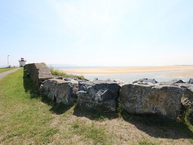 A stone wall and grassy path leading to a small lighthouse by a sandy beach at 5 Chandlers Yard in Burry Port
