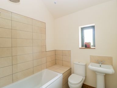 A bathroom with a bathtub shower combination a toilet a pedestal sink and a window with a small flower arrangement at The Milking Barn in Yeovil Somerset