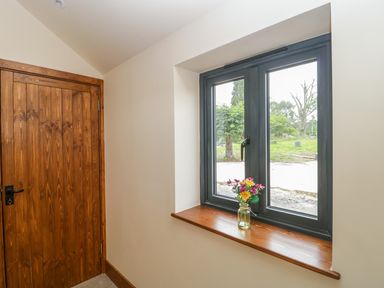 A window with a vase of flowers on the wooden sill and a closed wooden door in a room at The Milking Barn in Yeovil Somerset