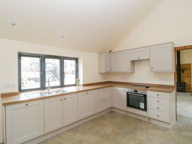 A kitchen with cupboards a sink an oven and a window with flowers on the counter at The Milking Barn in Yeovil Somerset
