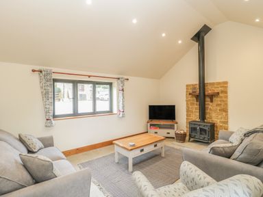 A living room with grey sofas a wooden coffee table a television and a wood stove with stone backdrop at The Milking Barn in Yeovil Somerset