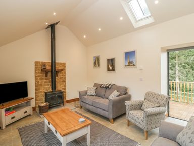 A living room with a sofa armchair coffee table wood stove TV and sliding door to balcony at The Milking Barn in Yeovil Somerset