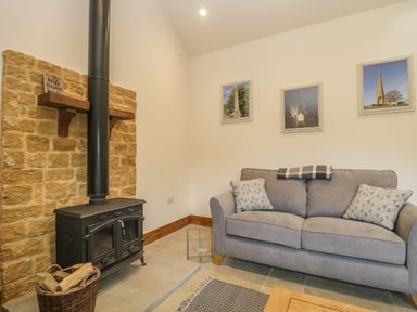 A living room with a wood burning stove couch and framed pictures on the wall at The Milking Barn in Yeovil Somerset