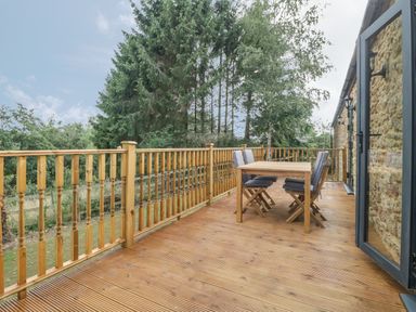A wooden deck with table and chairs overlooking trees at The Milking Barn in Yeovil Somerset