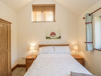 A bedroom with a bed between two bedside tables with lamps and a wooden wardrobe at The Milking Barn in Yeovil Somerset