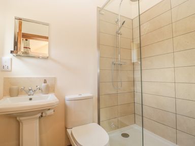 A bathroom with a pedestal sink, toilet, and a glass-enclosed shower with tiled walls at The Milking Barn in Yeovil Somerset